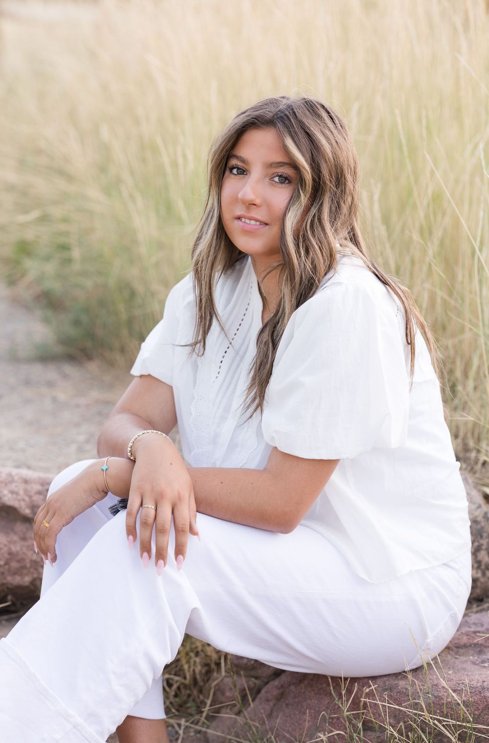 Lifestyle portrait of someone in an all-white outfit sitting casually in tall grass during golden hour.