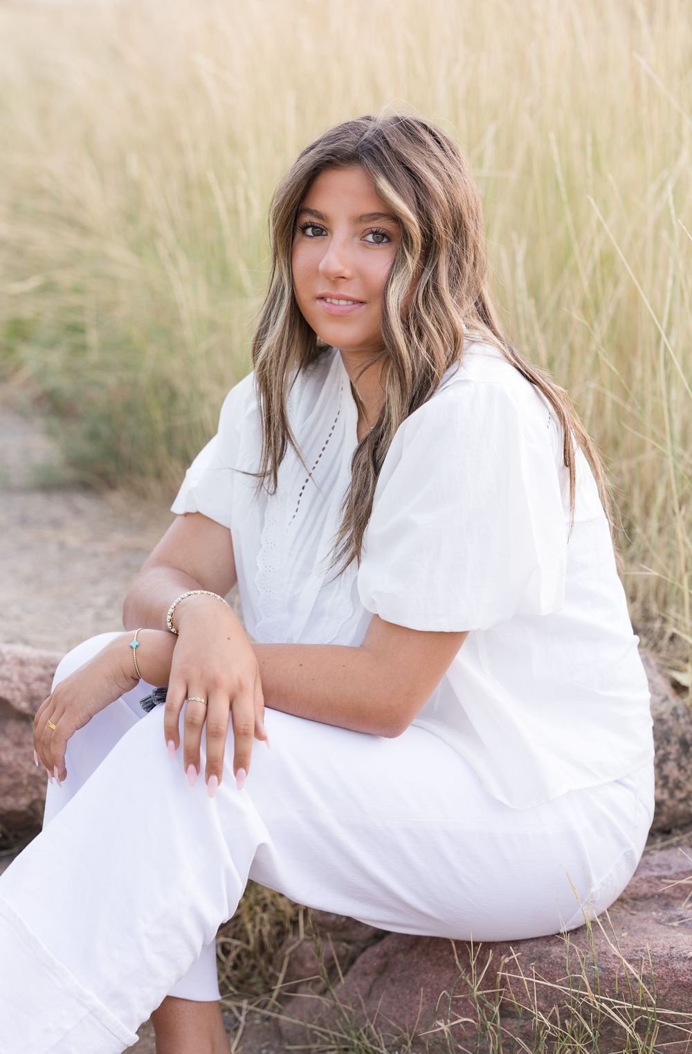 Portrait in a field featuring an all-white outfit with wavy hair against natural grasses.