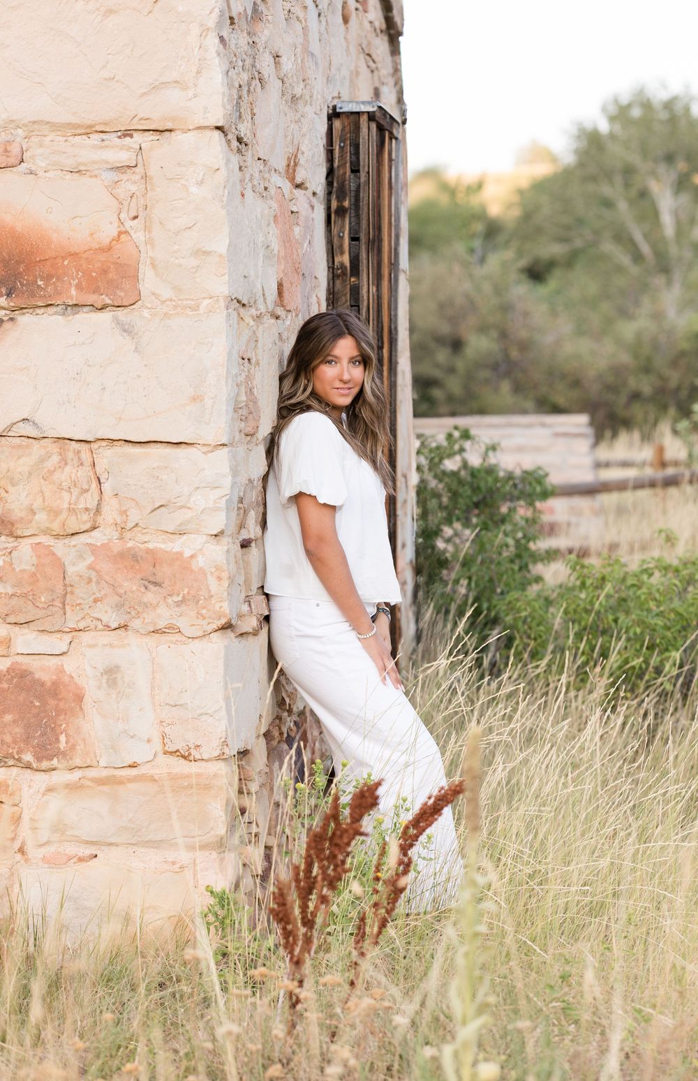 Stylish portrait against rustic stone wall surrounded by tall grass in natural lighting.