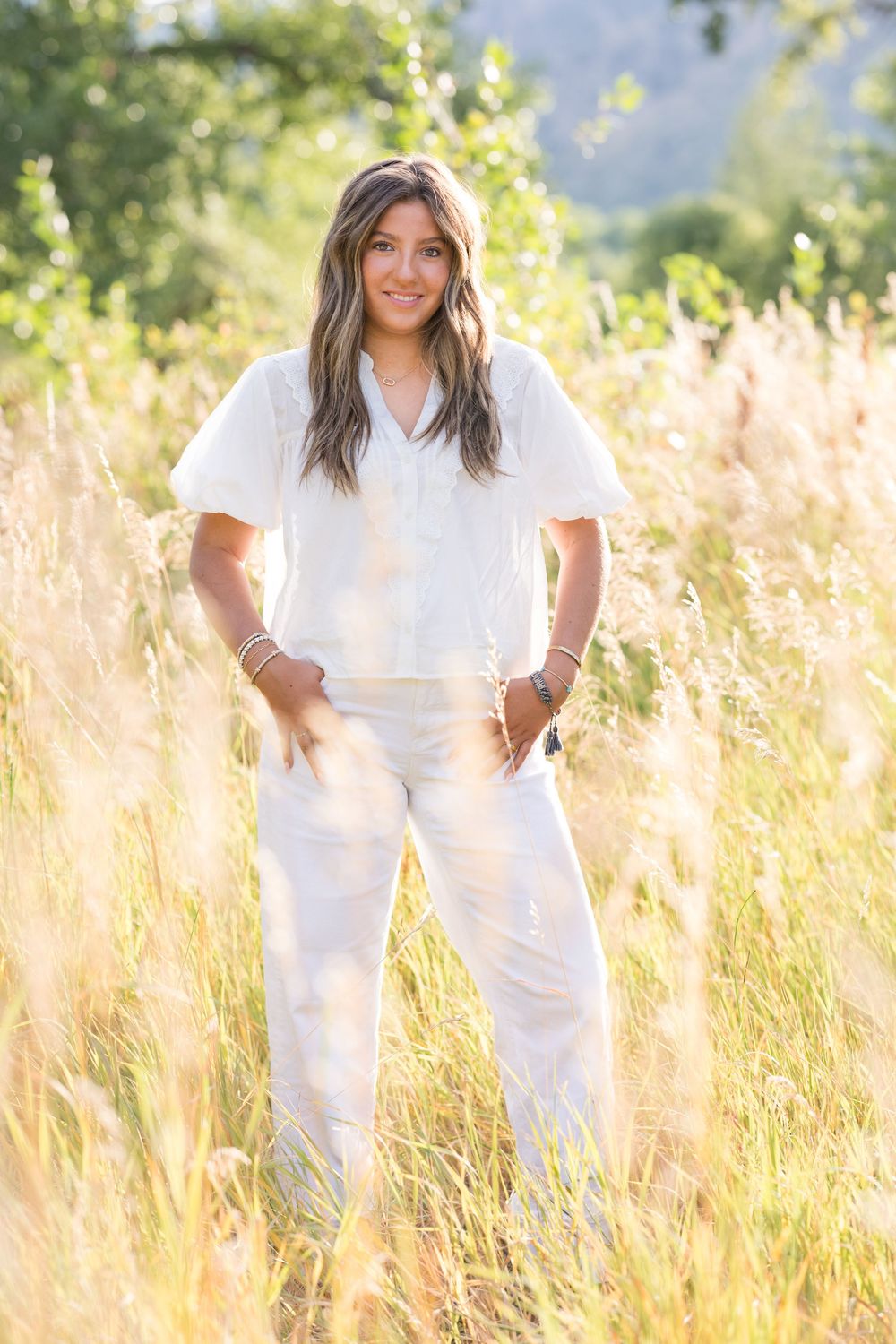Person in all-white outfit stands in sunlit meadow of tall golden grass during summer evening.