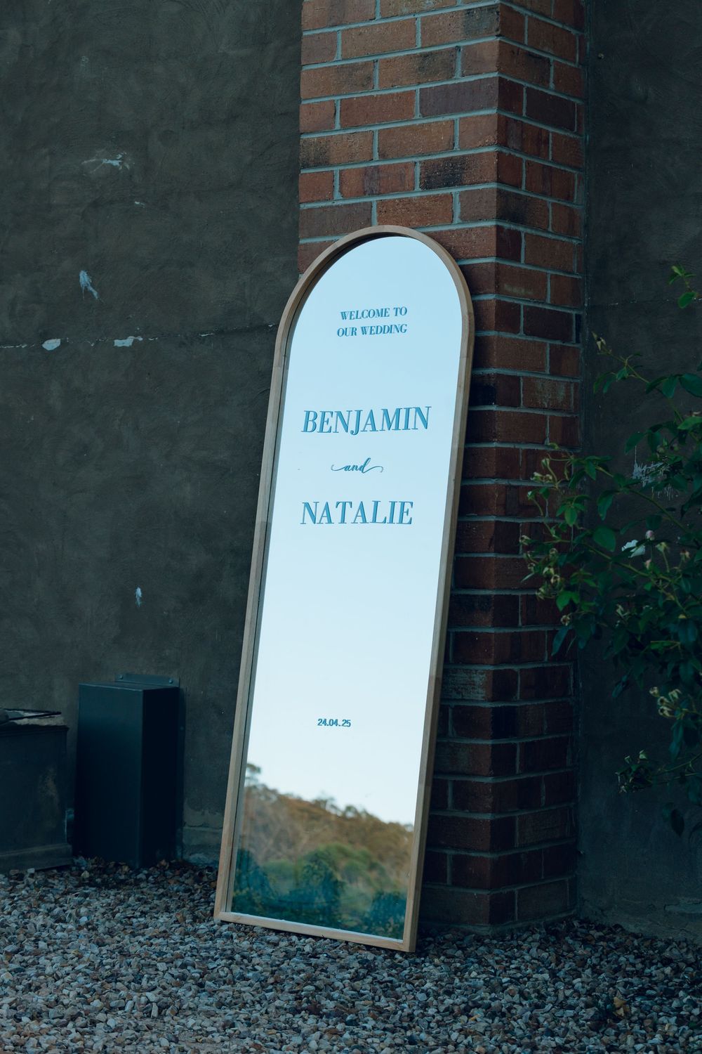 A decorative mirror with 'Benjamin and Natalie' text leaning against a brick wall.