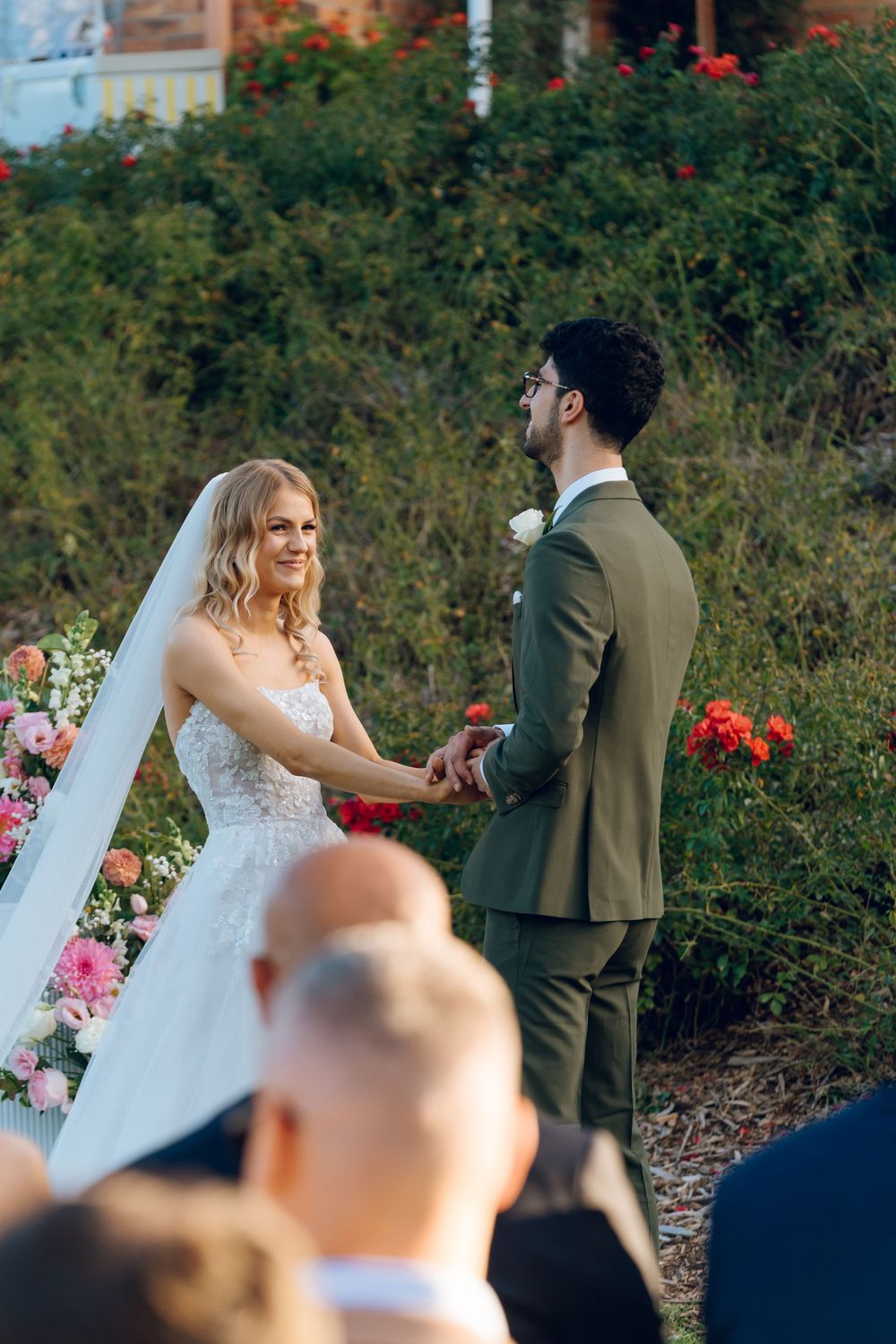 A wedding ceremony taking place in a garden with red flowers in the background.