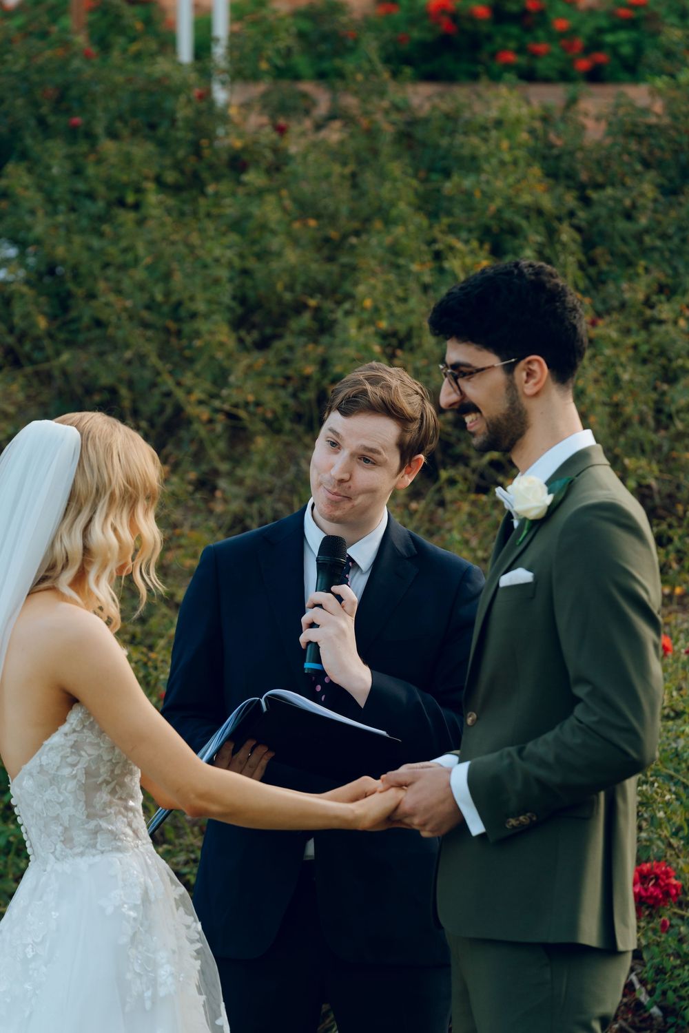 An outdoor wedding ceremony with officiant and couple exchanging vows among garden flowers.