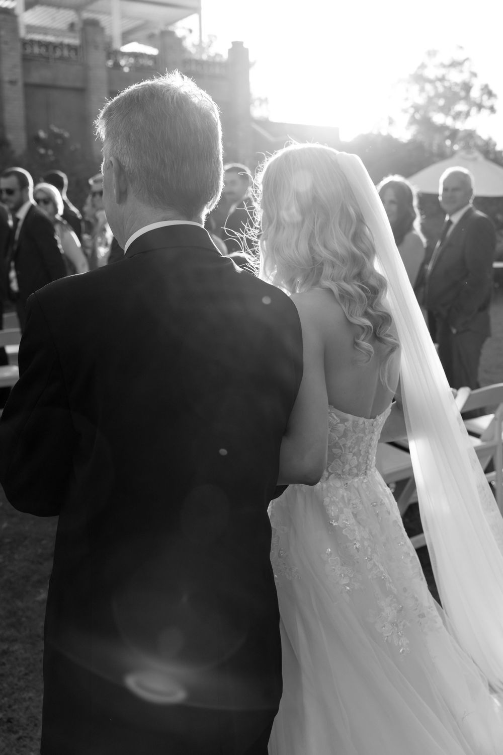 Black and white photo of wedding couple walking among guests during outdoor ceremony.