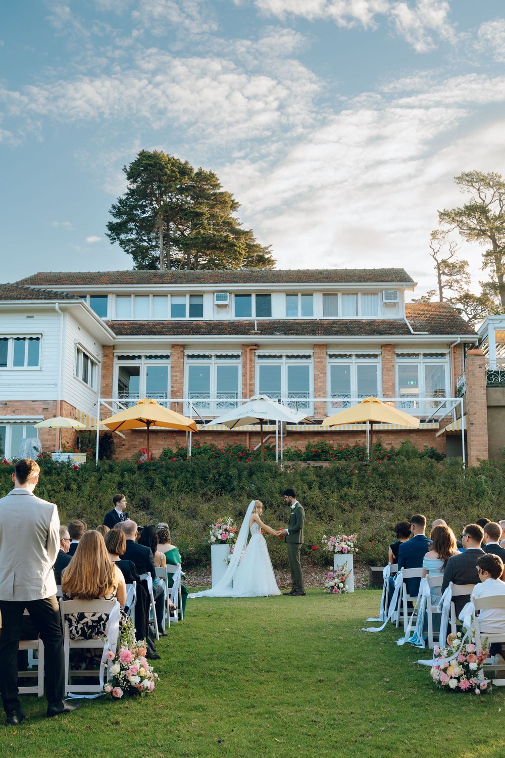 Outdoor wedding ceremony setup with white chairs and floral arrangements in front of modern building.