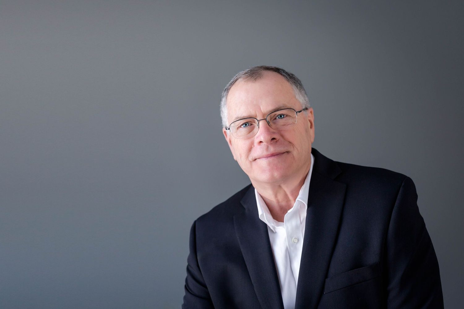 Professional profile portraits of a businessman in a dark suit against a gray background.