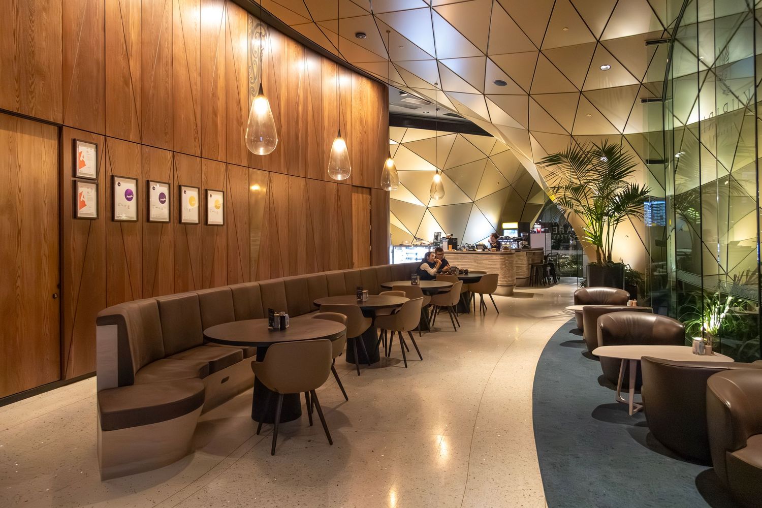 Sleek cafe interior with warm wooden walls, gold faceted ceiling panels, and globe pendant lights.