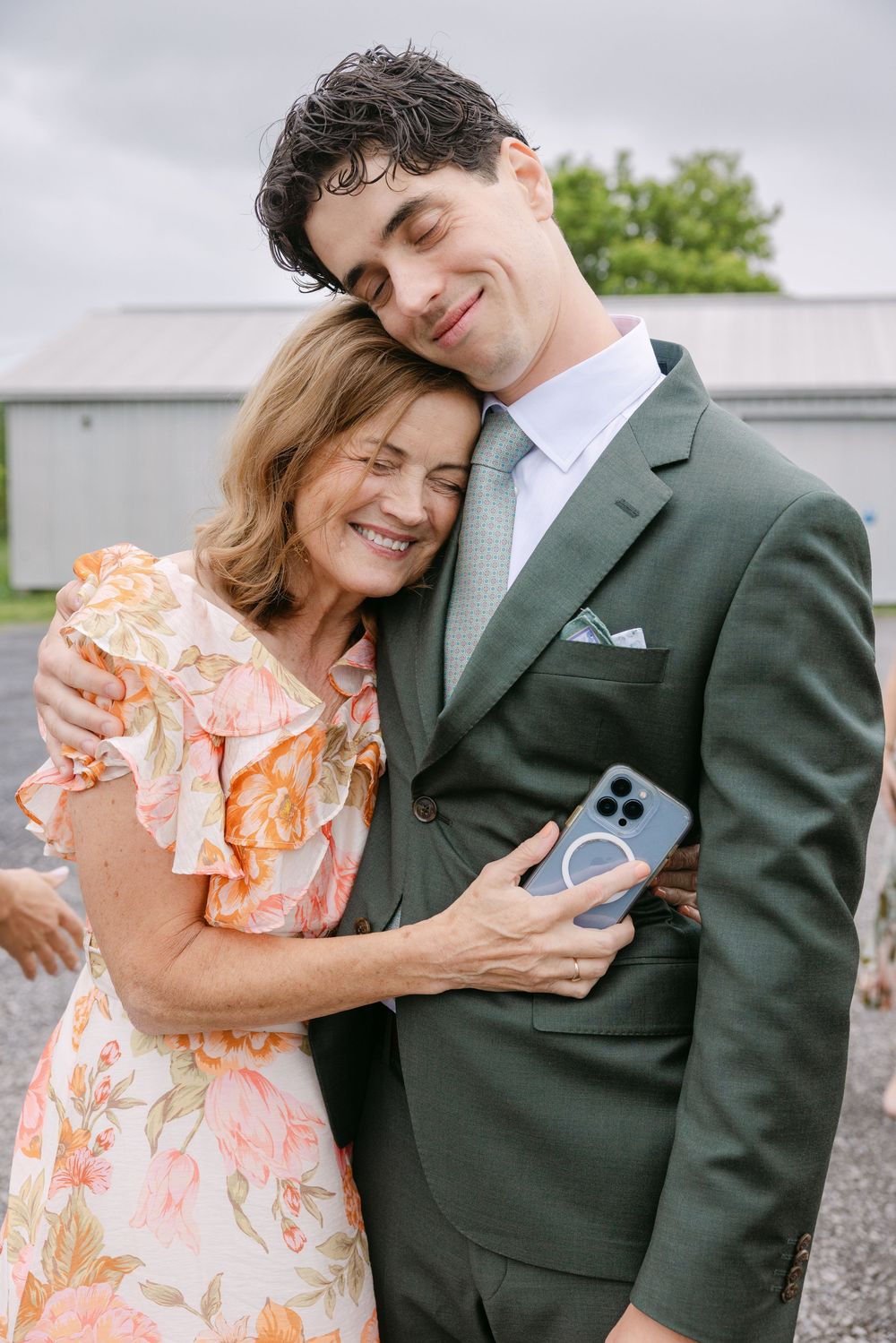 A couple in formal attire share a tender embrace, with her wearing a floral dress and him in a dark green suit.