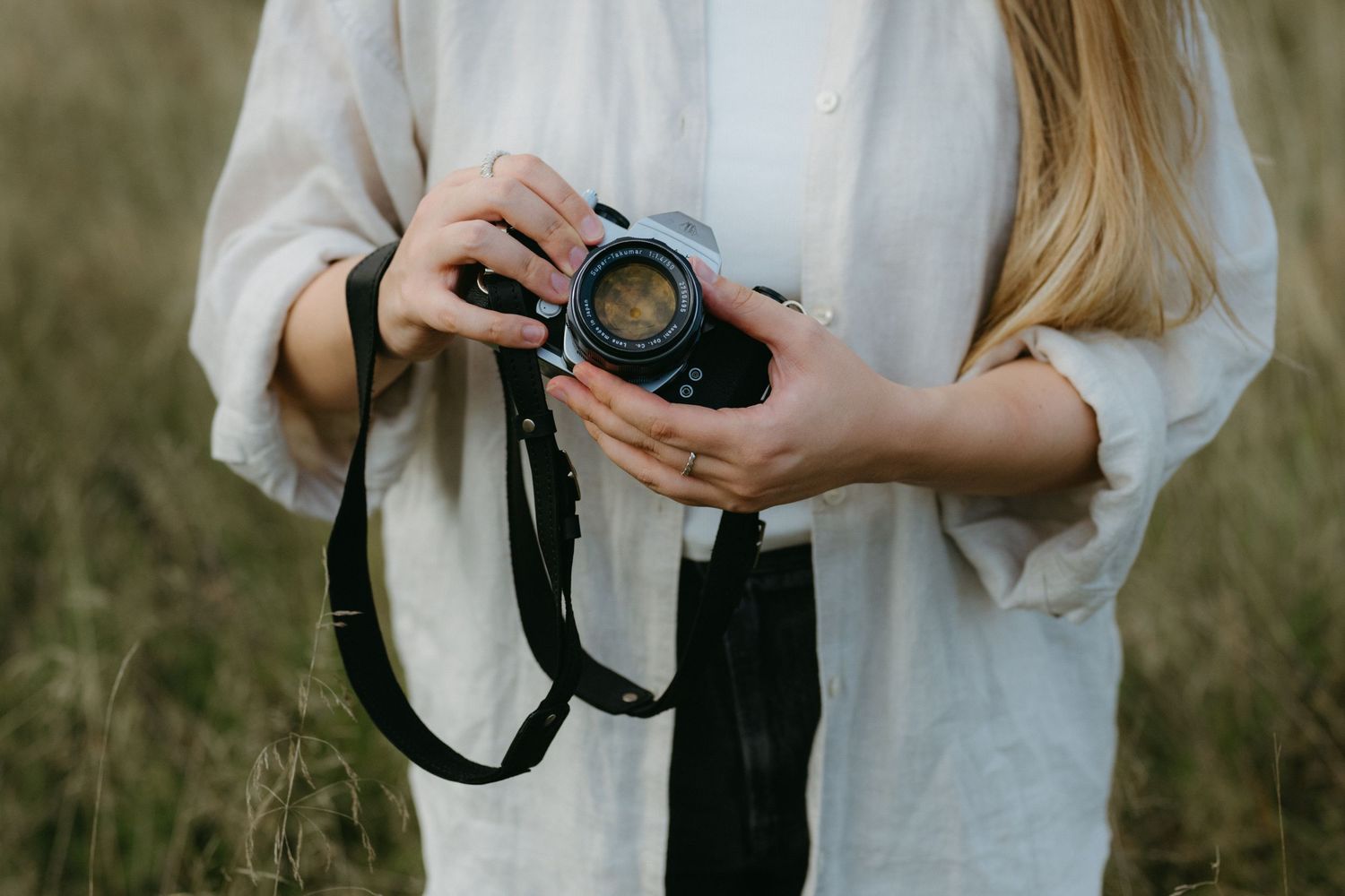 Someone in a light colored shirt holds a professional camera while photographing outdoors in a field during golden hour.