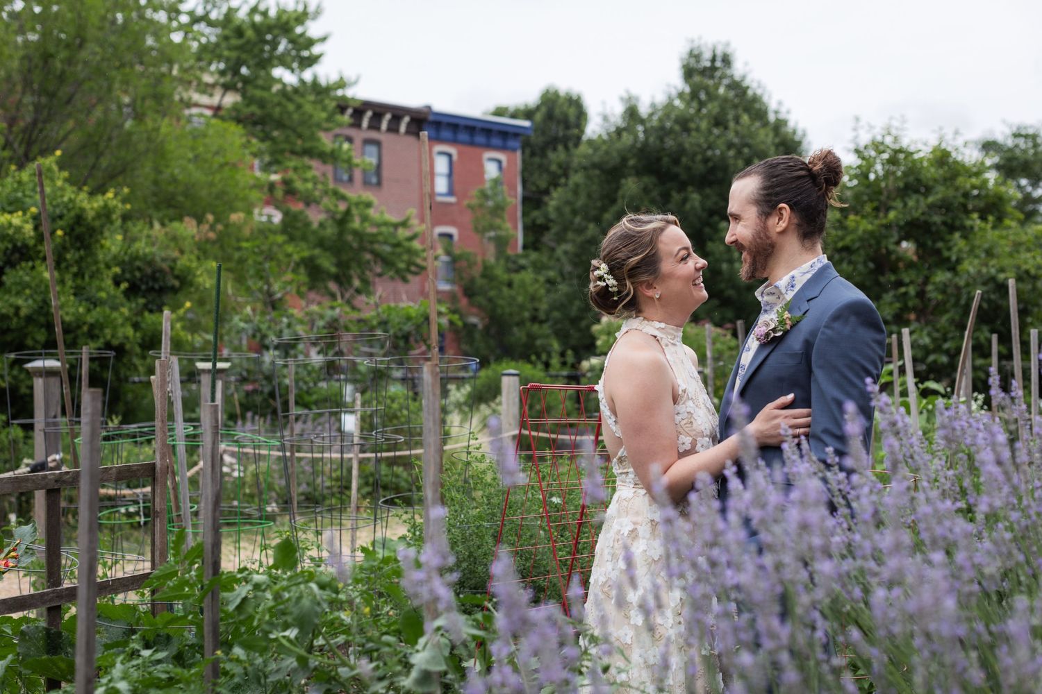 A couple shares a romantic moment in a garden with purple delphinium flowers blooming in the foreground.