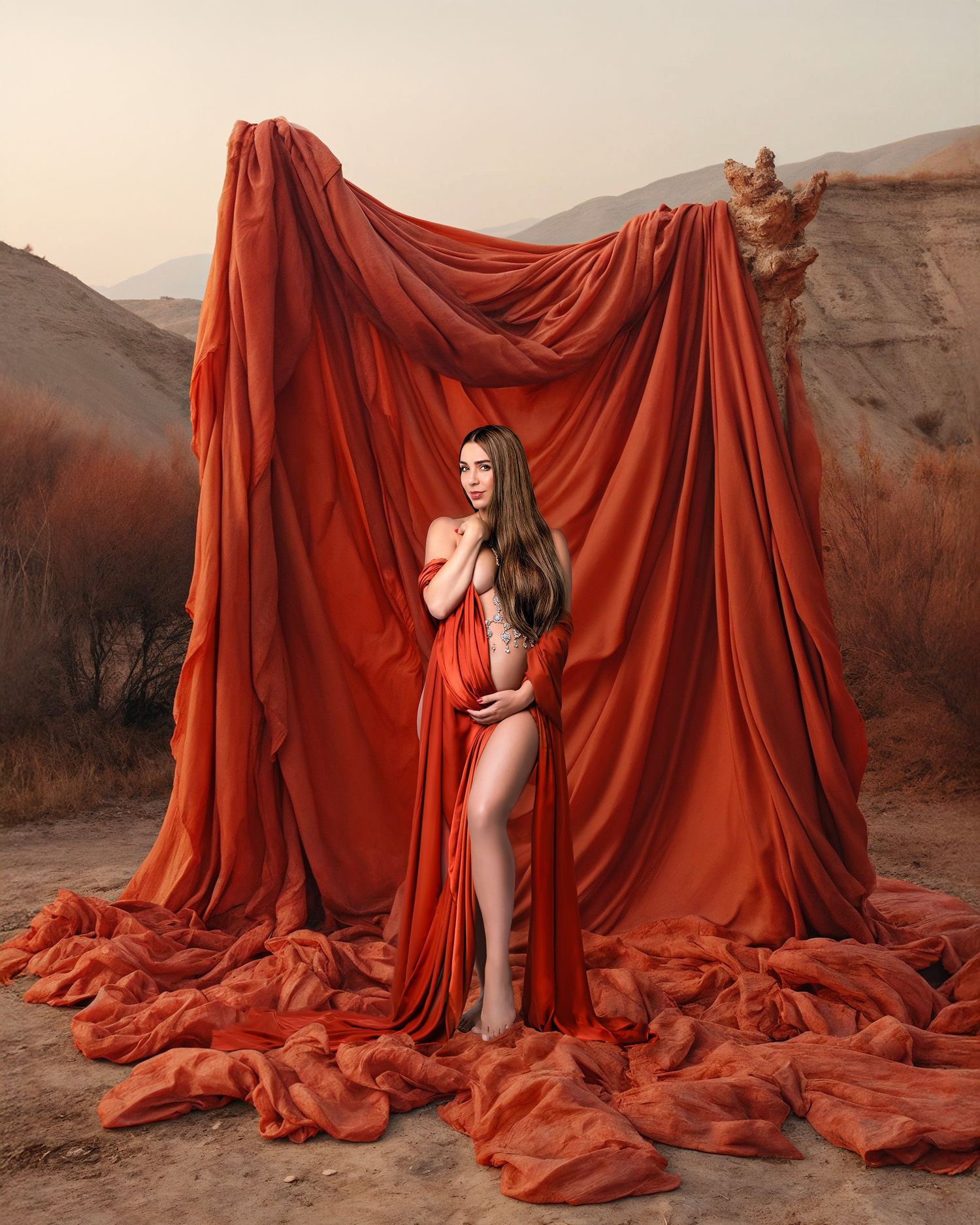 Pregnant woman embracing her baby bump draped in rust coloured silk against a beautiful desert scene. Photographed by Caz Captures in Sydney