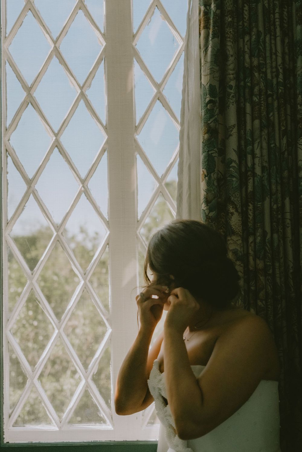 Bride in front of large window putting earrings in Lafayette event space