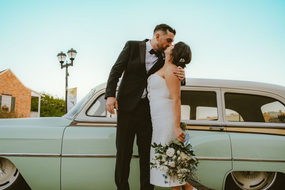 Bride and groom kissing in front of vintage car Lafayette event space