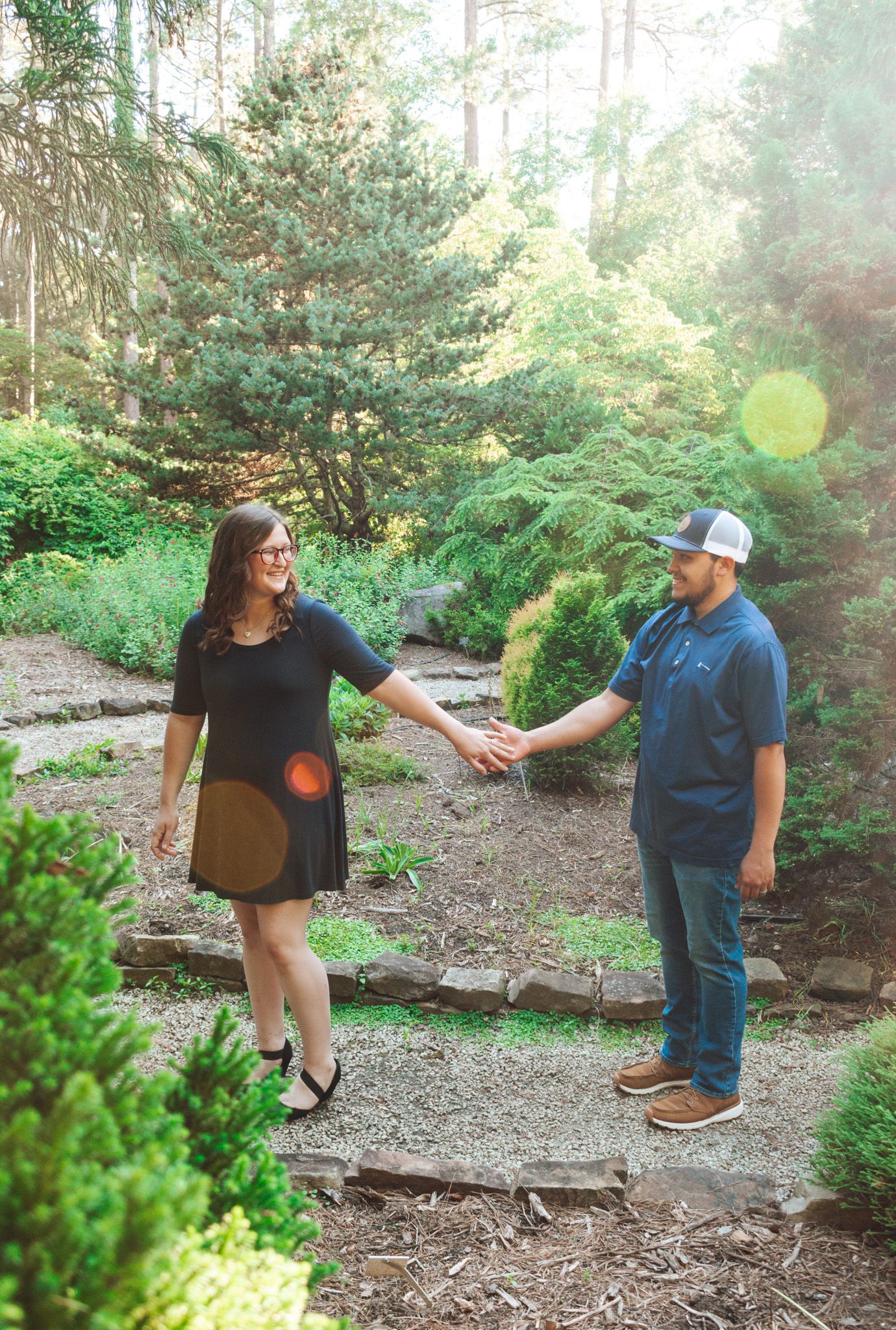 A couple holding hands while walking on a forest trail surrounded by evergreen trees.