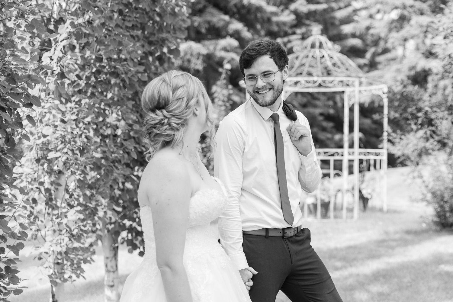 Black and white wedding photo showing joyful moment in garden with gazebo.