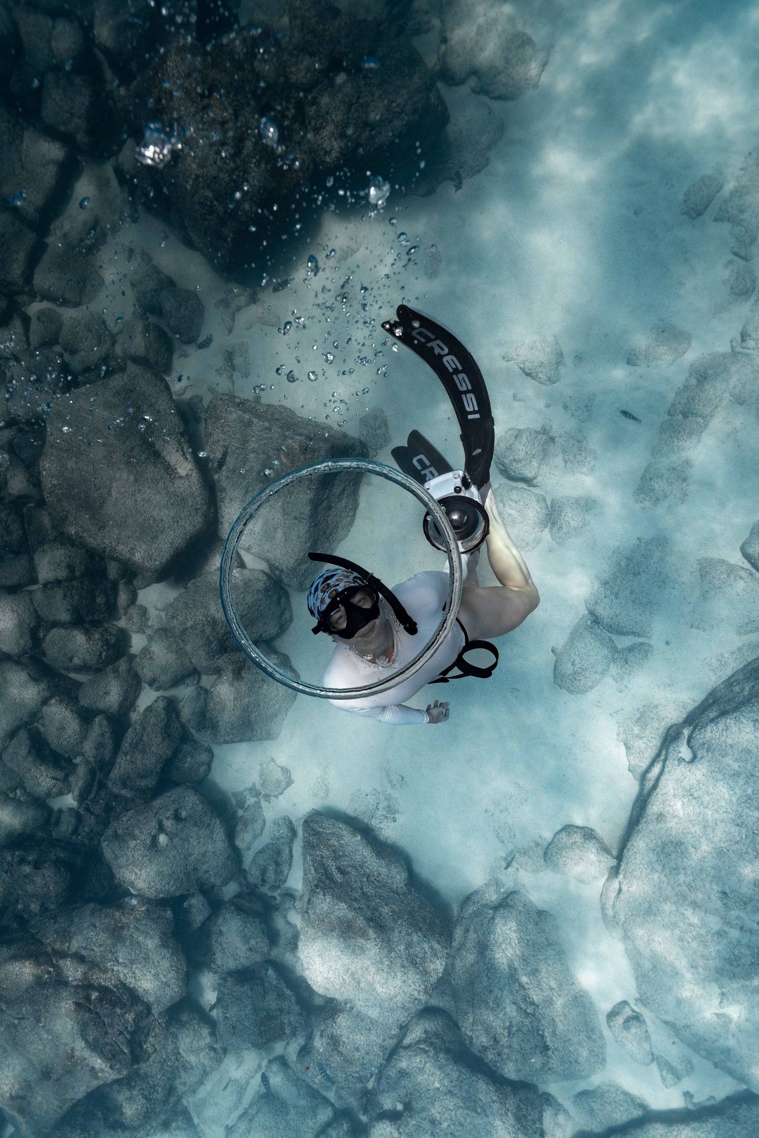 Overhead view of Gaby Salvador exploring rocky underwater terrain, framed by a bubble ring, in the Galapagos.