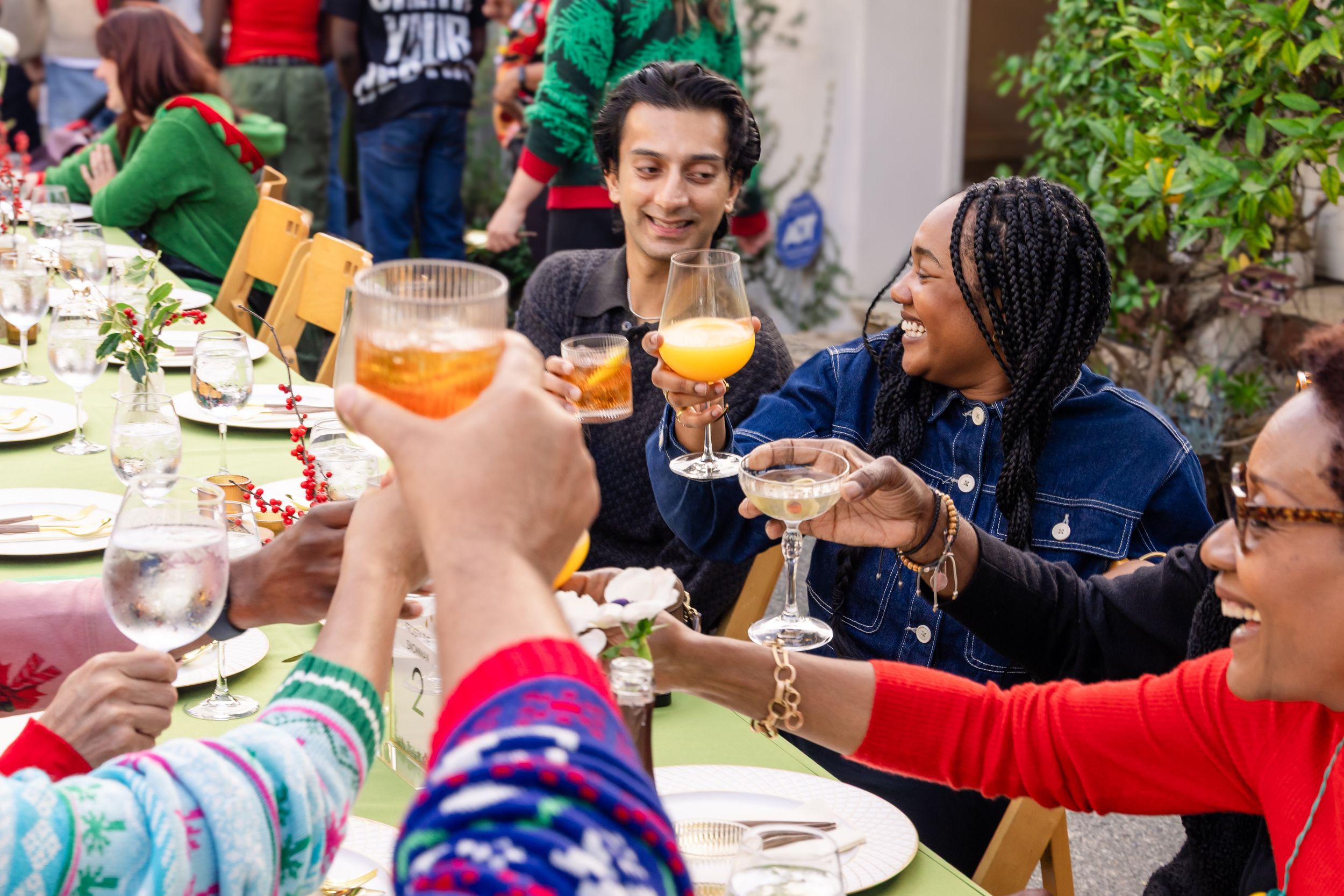 Diverse group of friends toasting with colorful cocktails at festive outdoor holiday dinner.