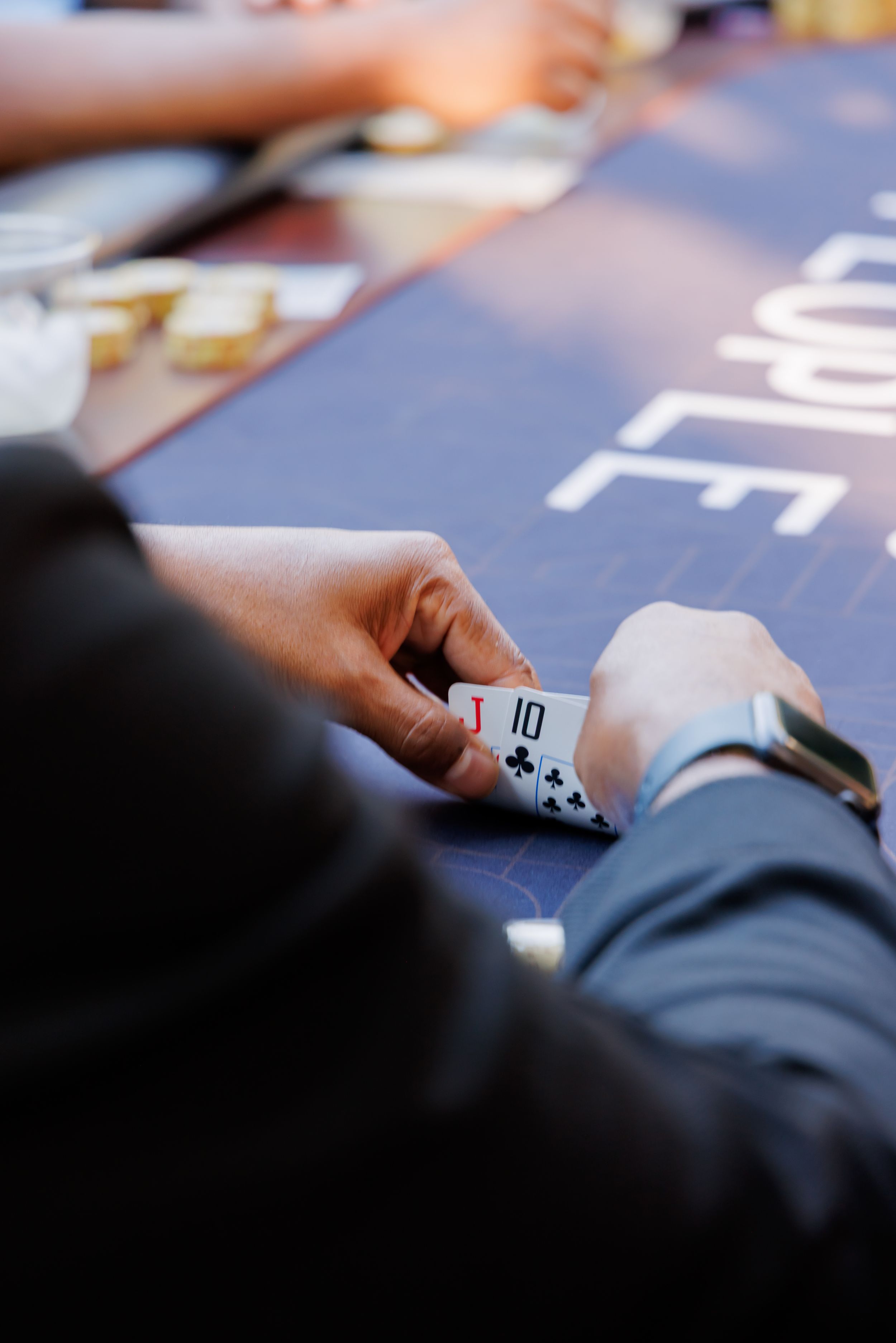A poker player holds playing cards showing a 10 of clubs at a casino card table.