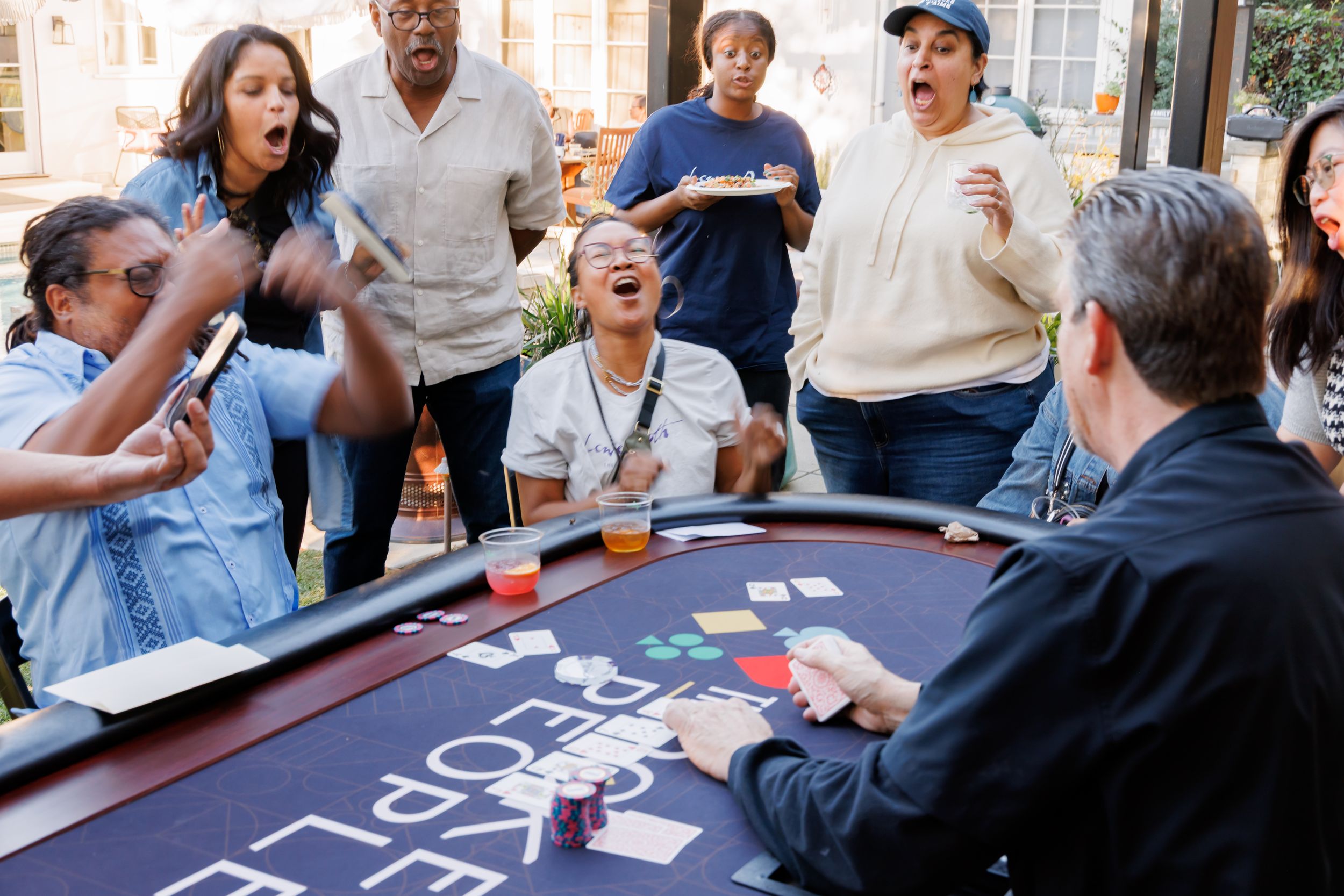 Excited group of people reacting at poker table during lively outdoor casino party event.