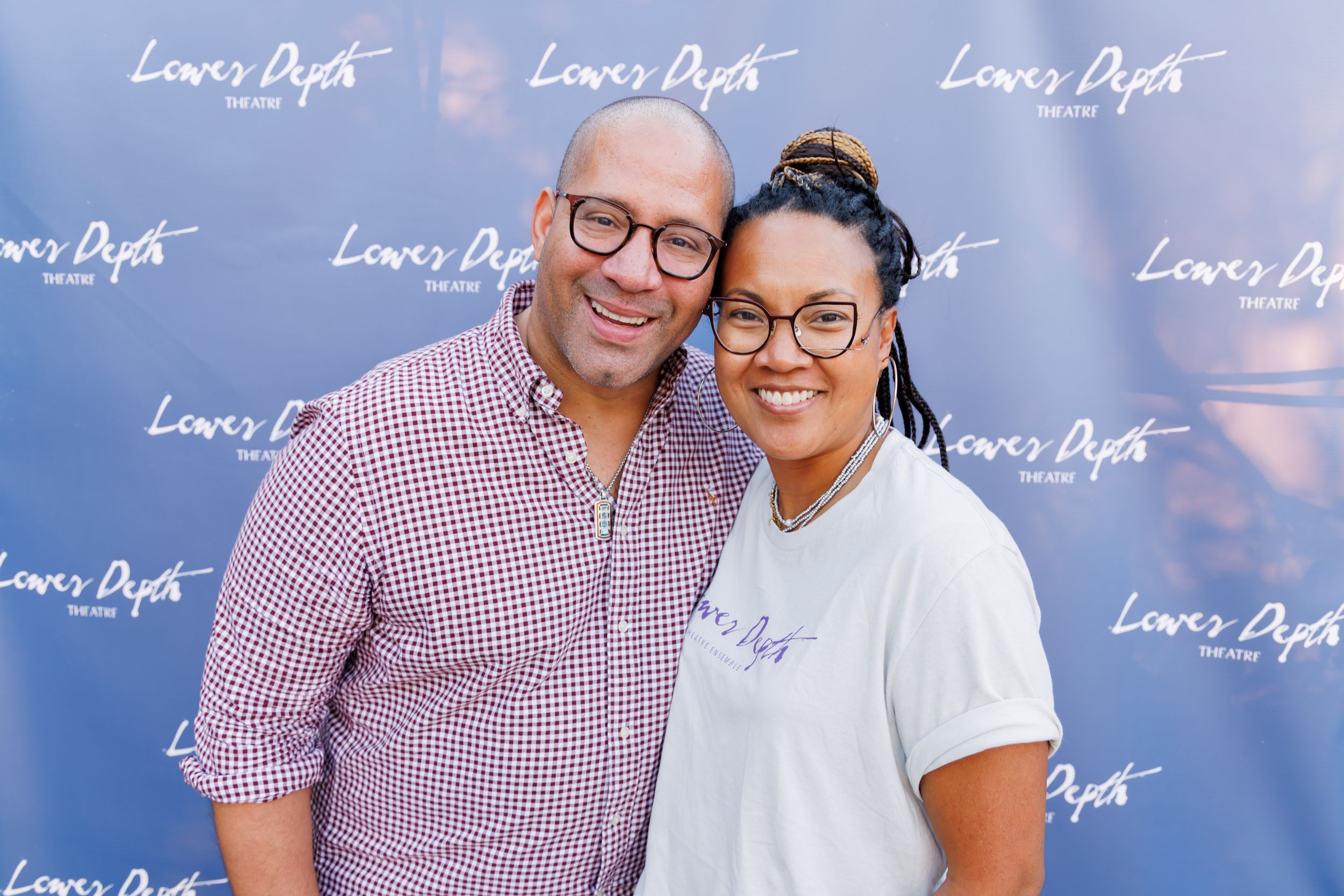 Smiling couple posing together in front of Lower Depth branded step-and-repeat backdrop.