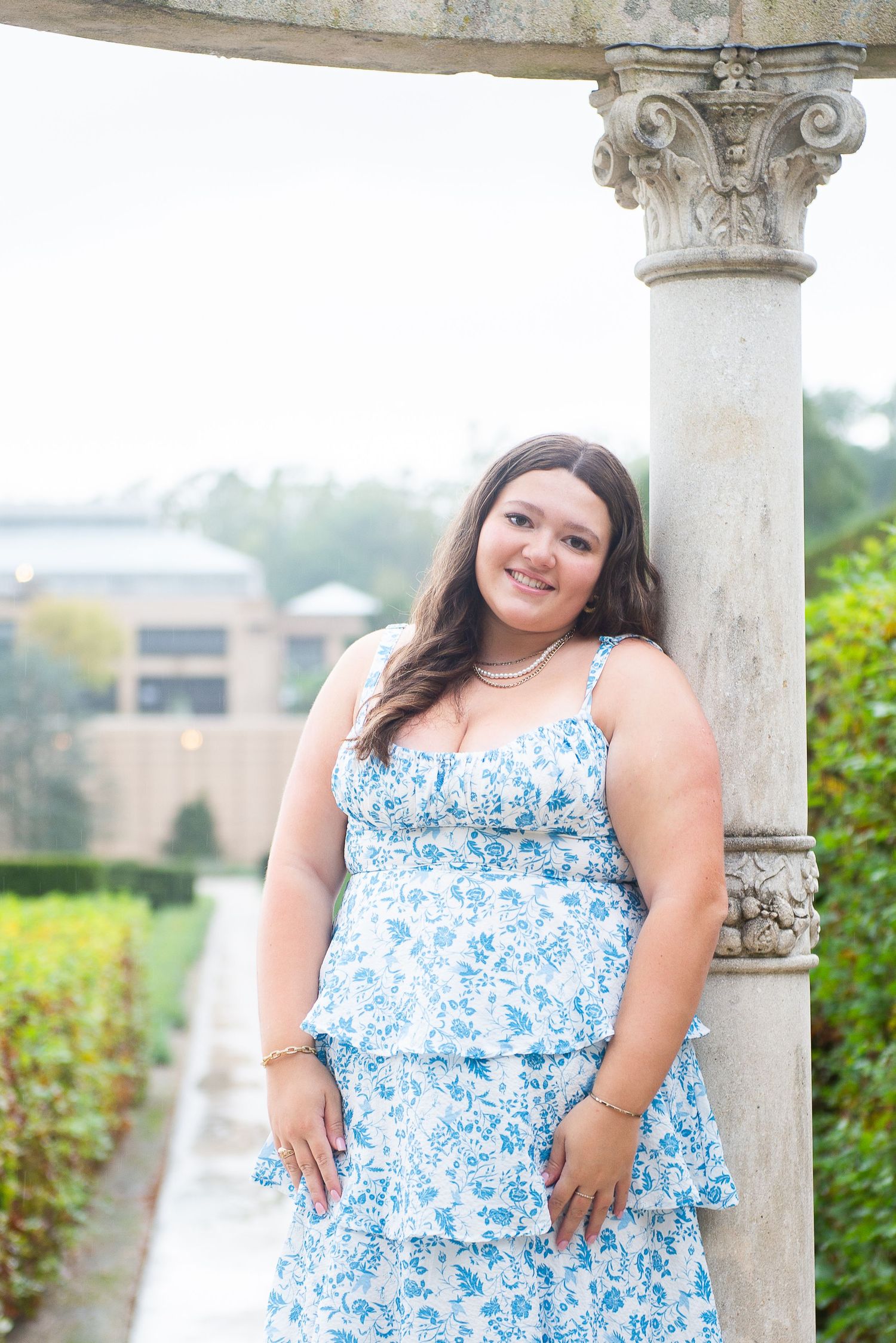 A floral blue and white tiered dress is worn elegantly next to an ornate architectural column during a senior session at Longwood Gardens.