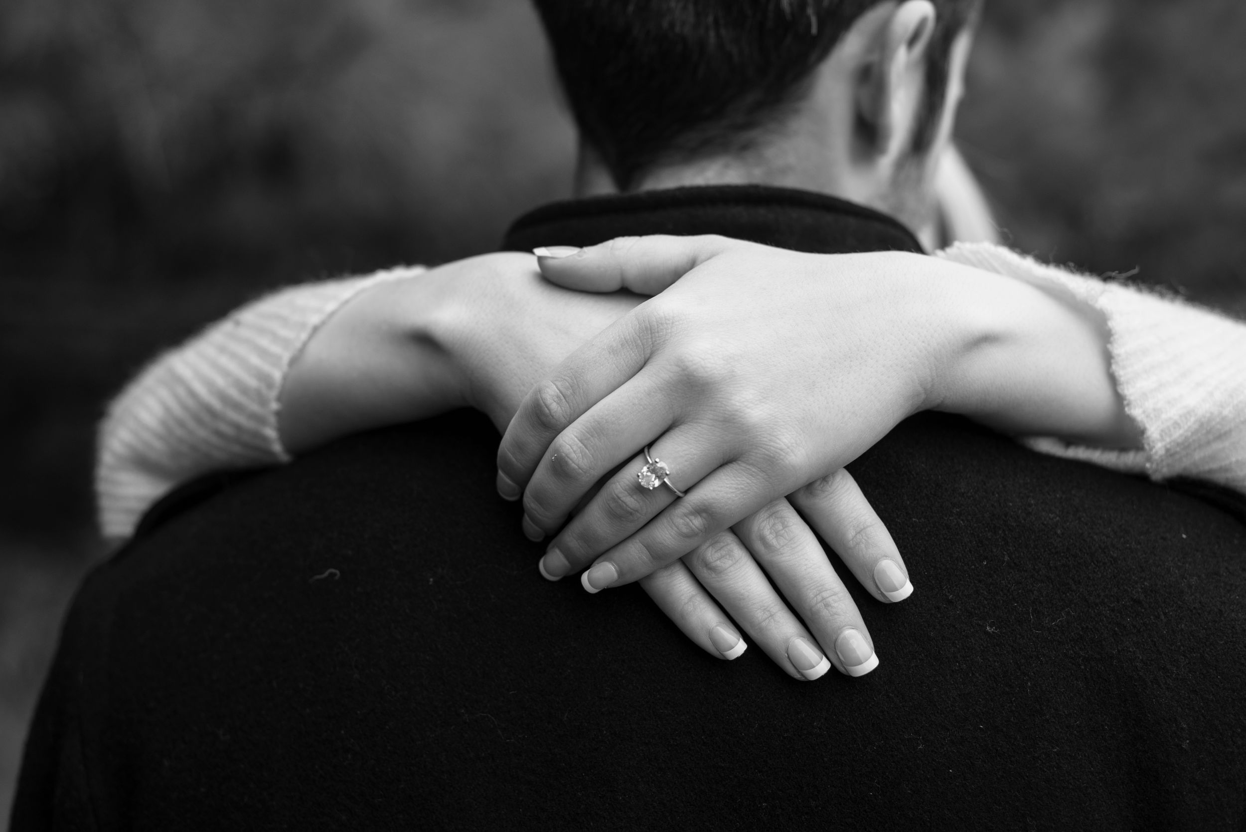 Black and white photo showing hands with engagement ring embracing during romantic moment.