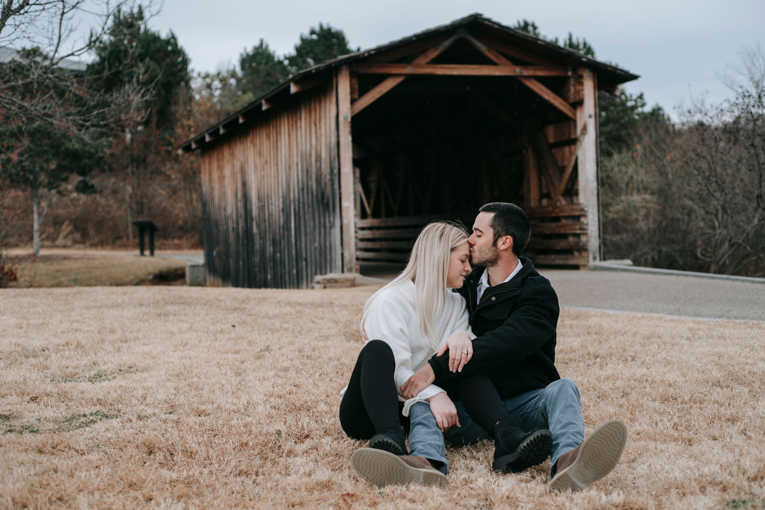 Intimate moment captured between couple sitting by rustic covered bridge during engagement photos.