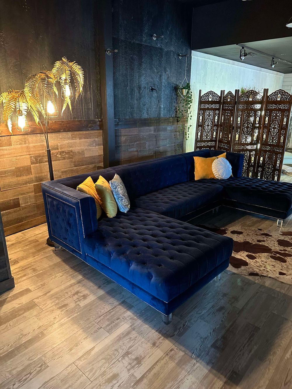 Dark blue tufted velvet chaise lounge against wood paneled wall with hanging pendant lights.