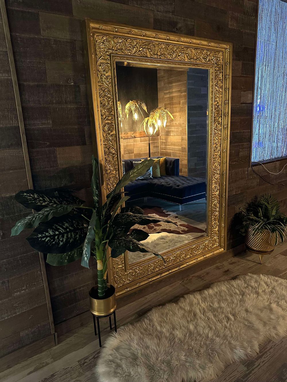 Ornate gold-framed mirror mounted on dark wood wall with decorative plants.
