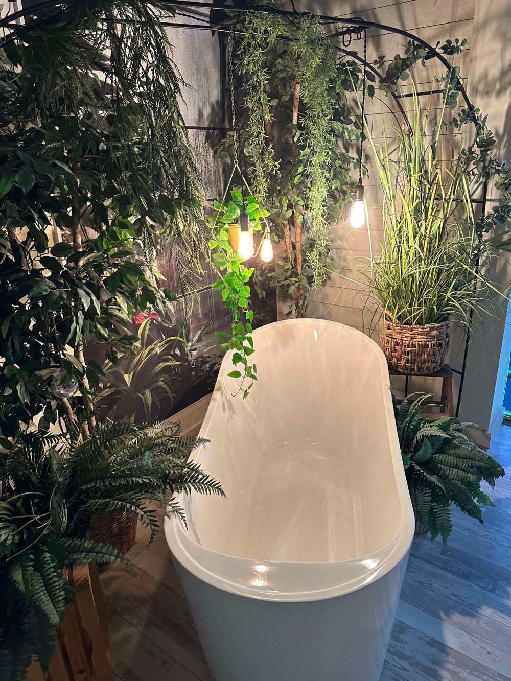 White freestanding bathtub surrounded by lush tropical plants and ambient lighting.