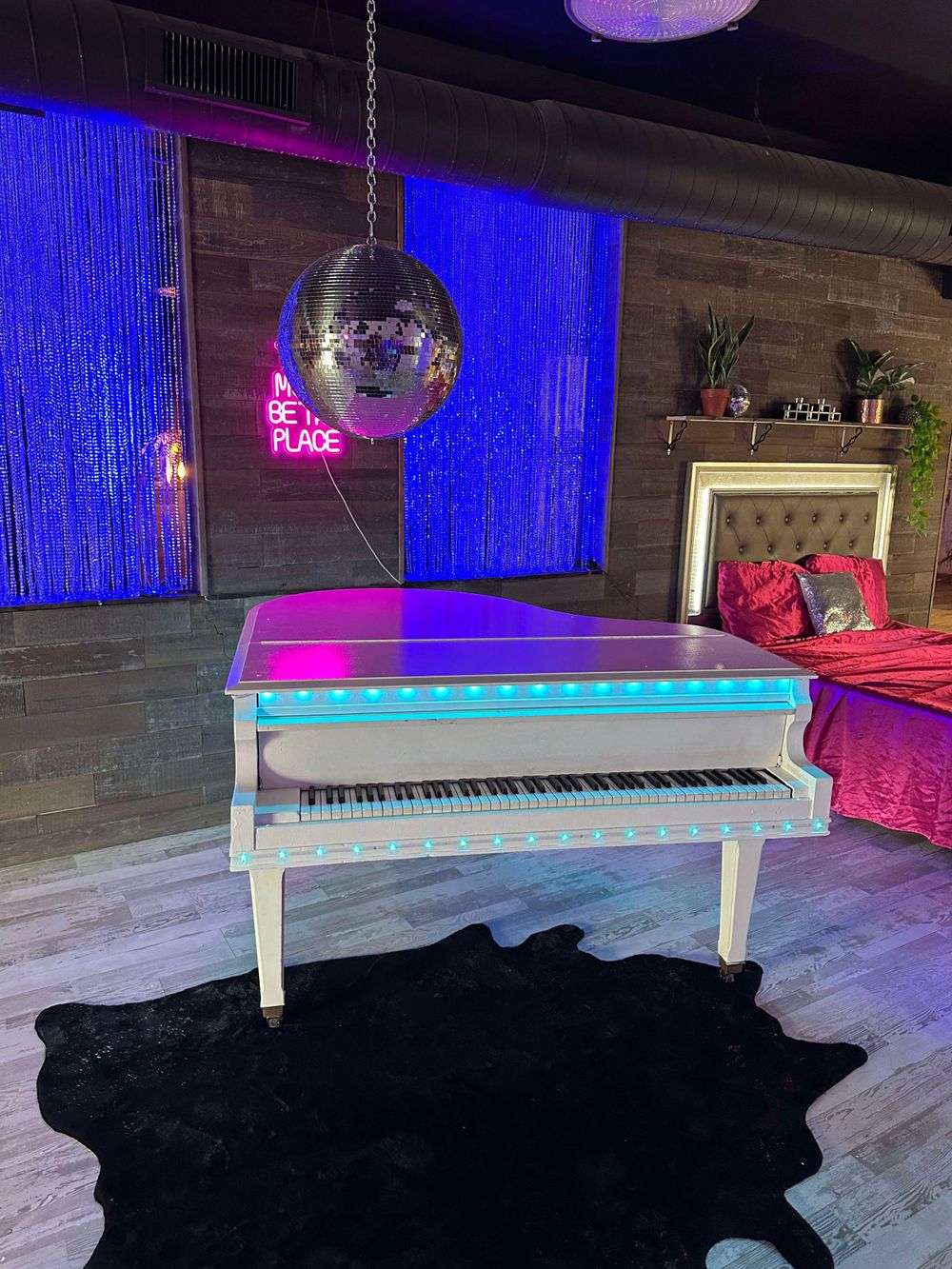 White piano on black cowhide rug with blue neon lighting and disco ball ambiance.