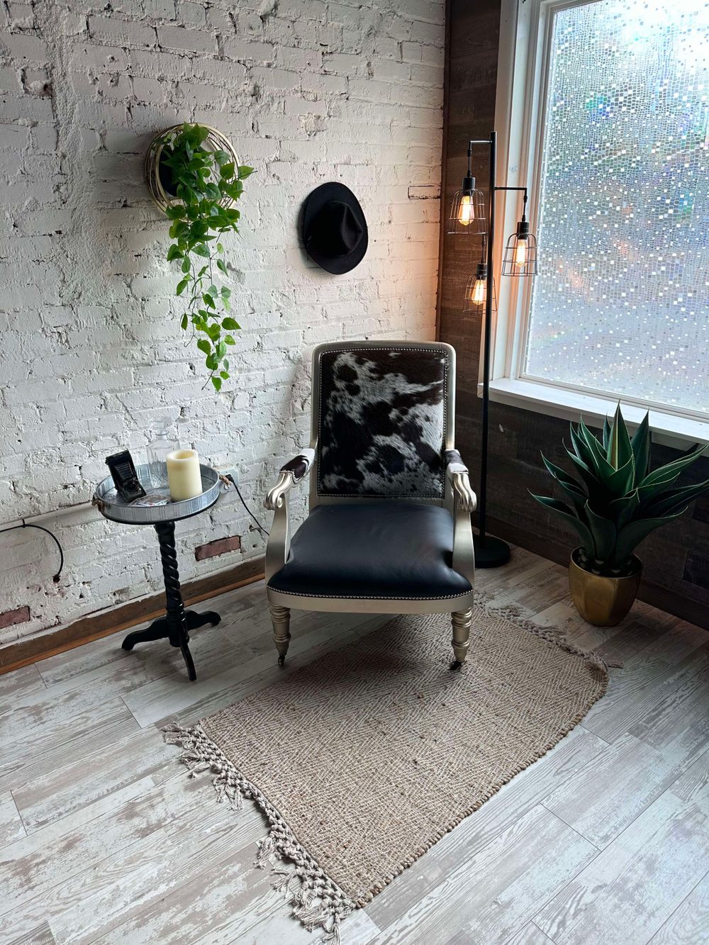 Minimalist seating area with gray chair, plants, and white brick walls near window.