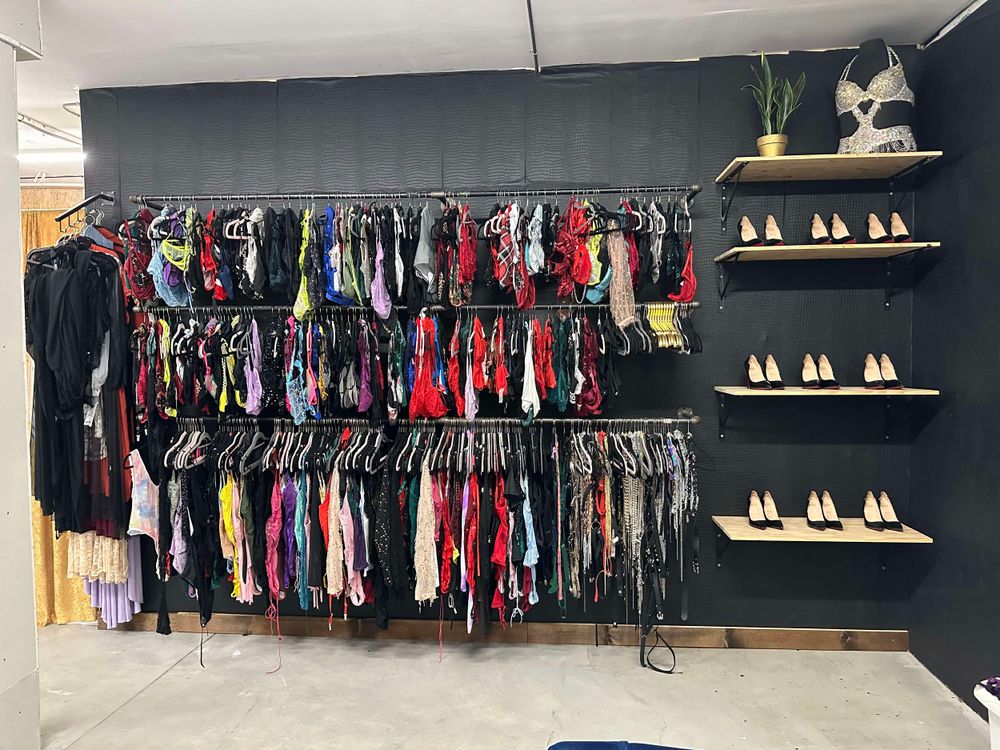 Retail clothing store interior with racks of colorful garments and red bottom heels display on wall shelves. Size inclusive client closet.