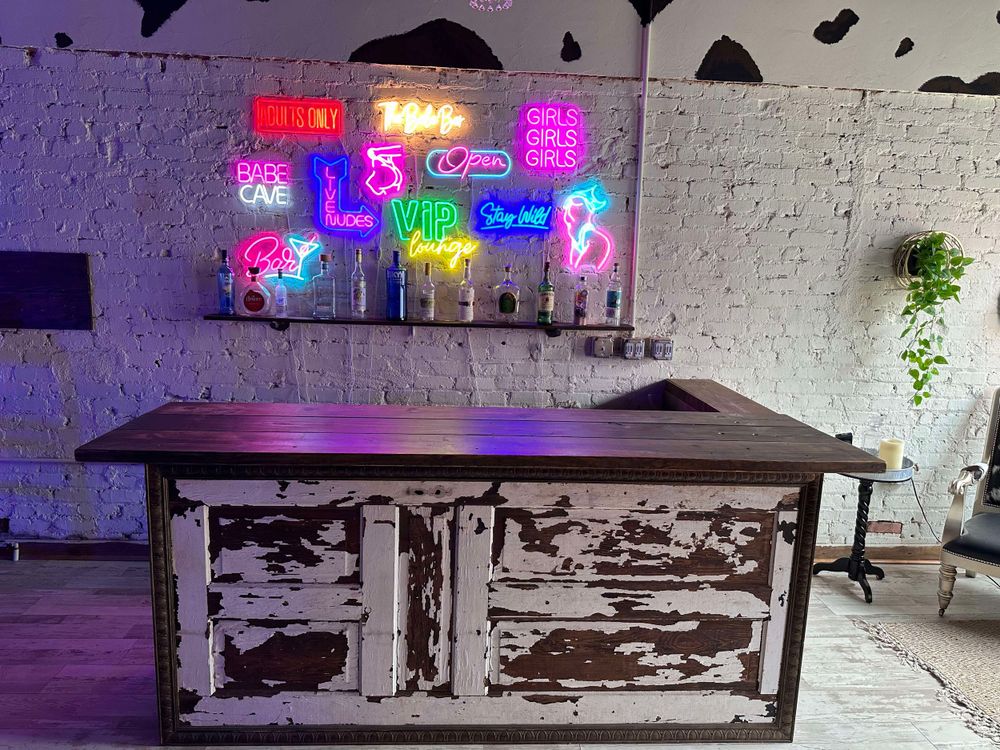 Distressed vintage cabinet with neon signs mounted above against white brick wall.