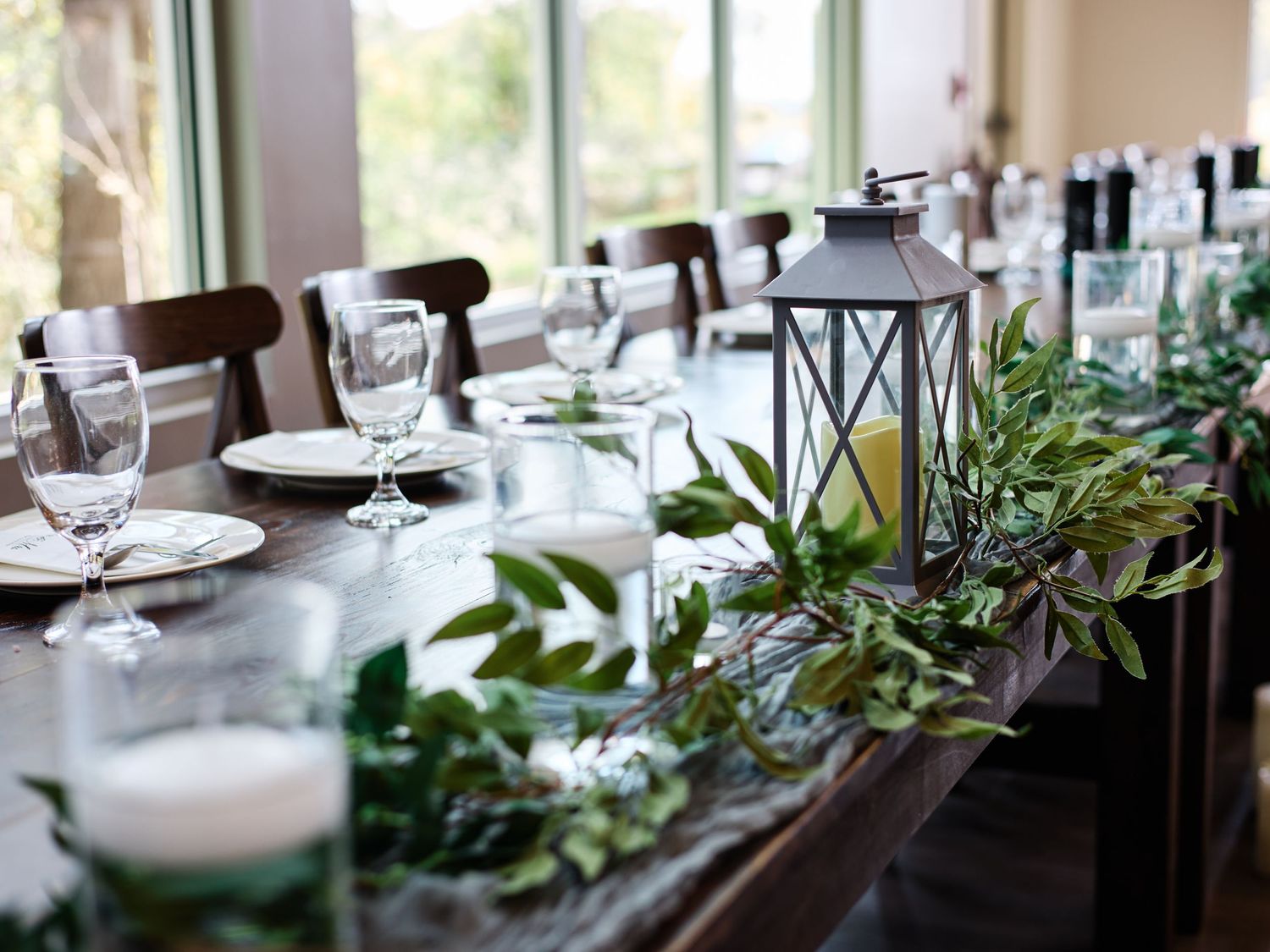 Elegant table setting with lantern centerpiece and greenery garland for wedding reception.