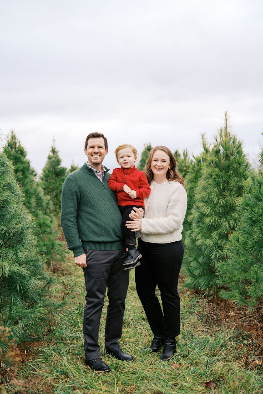 Family poses together at Christmas tree farm surrounded by young pine trees.