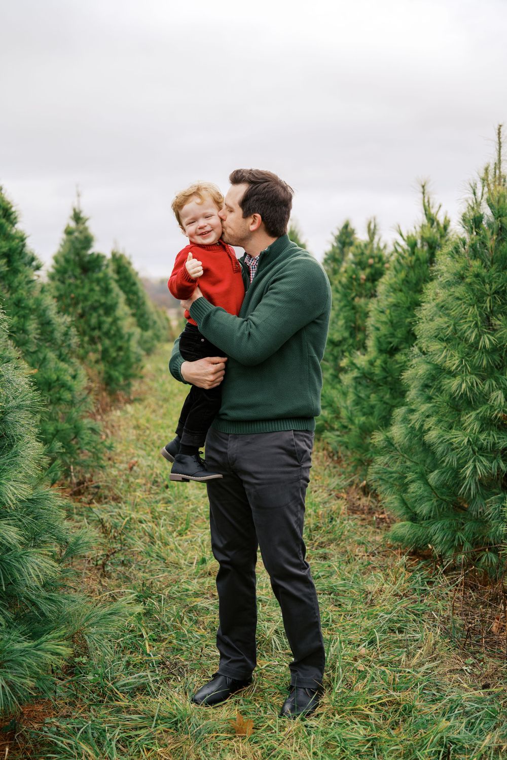 Parent lifts child playfully while family enjoys time at Christmas tree farm.