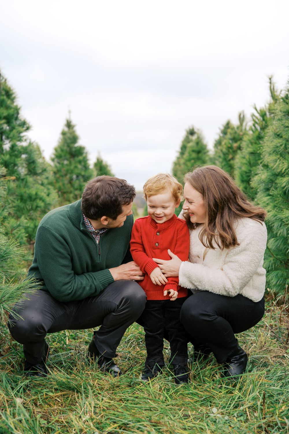Intimate family moment shared between three people crouching among evergreen trees.