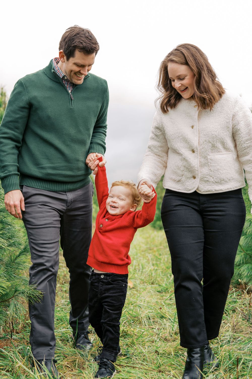Family walking together through a Christmas tree farm while holding hands.