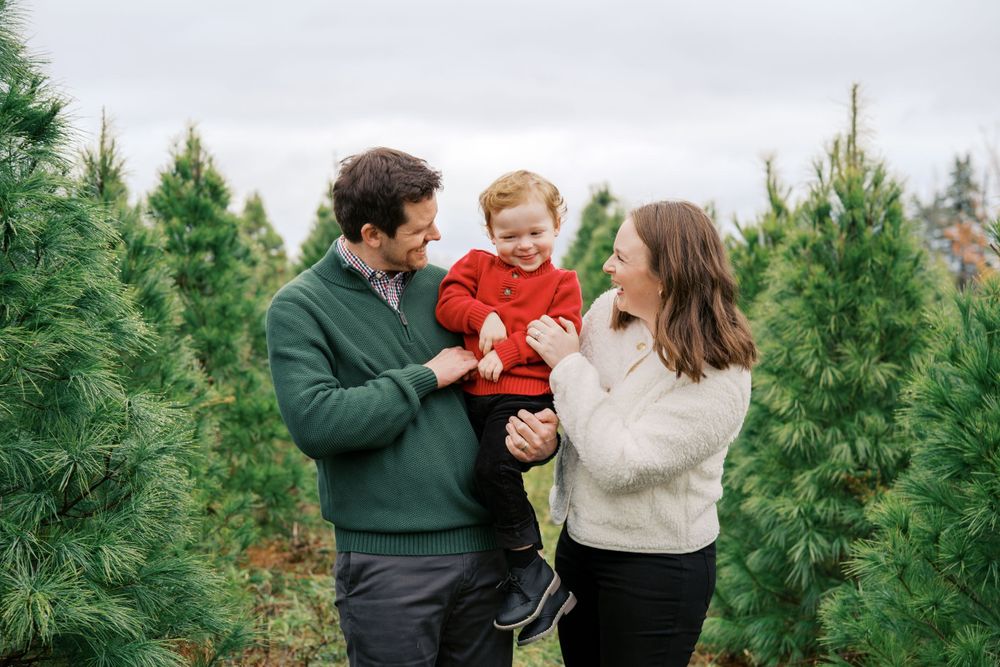 Family shares joyful moment among rows of evergreen trees at tree farm.