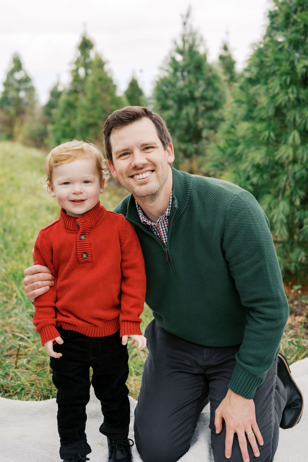 A parent and child smile together while posing at a Christmas tree farm.