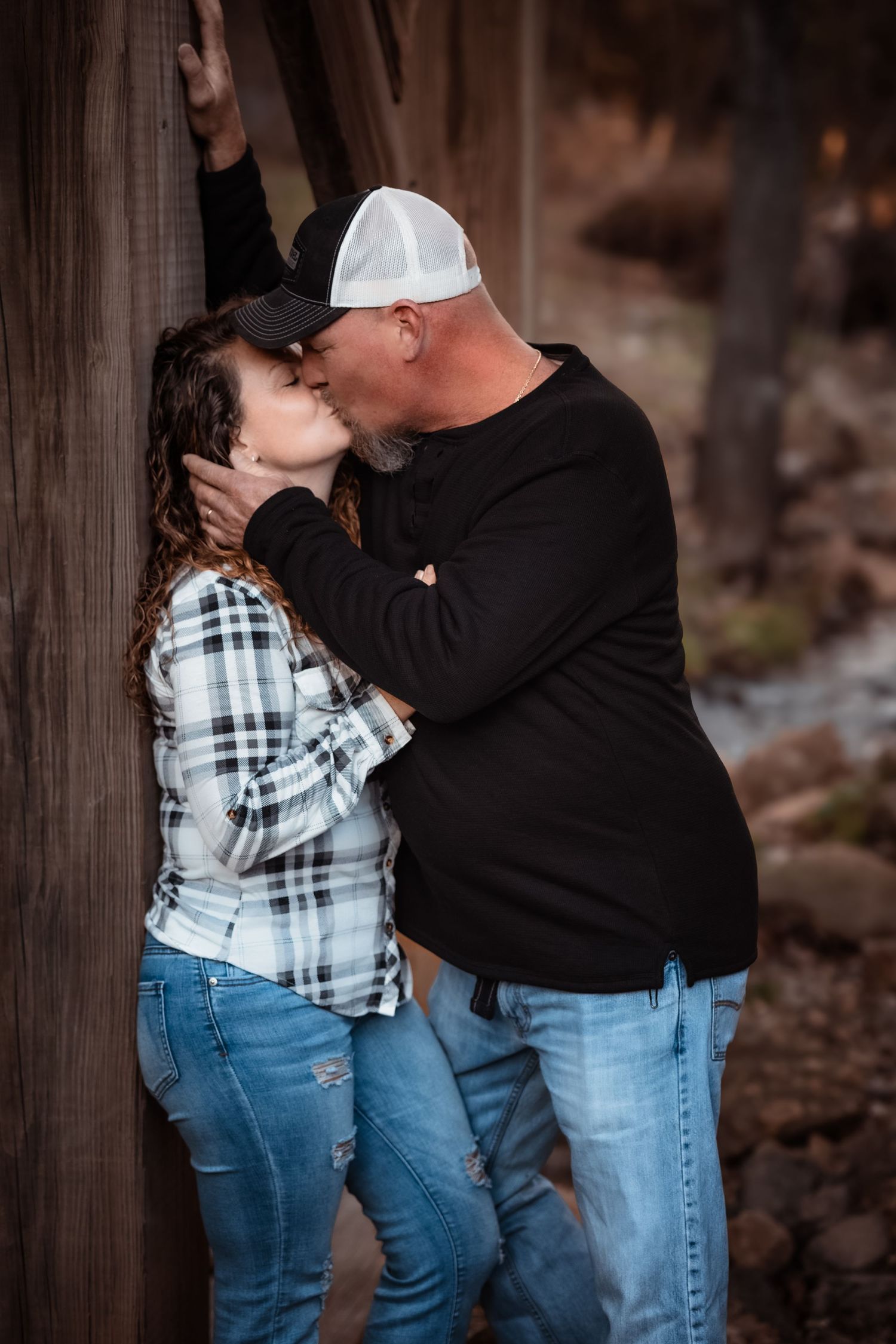 Romantic couple sharing intimate moment against wooden wall outdoors.