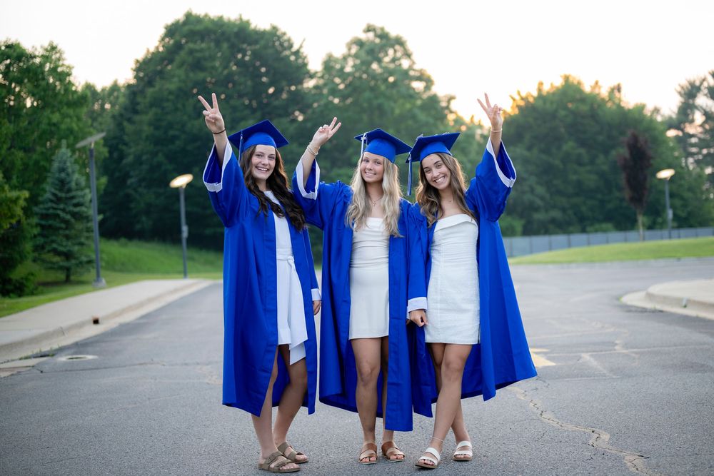 Graduates in blue caps and gowns pose together outdoors during sunset celebration photoshoot.