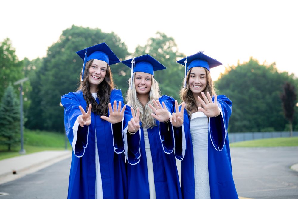 Friends in blue graduation attire celebrate together in a parking lot during golden hour.