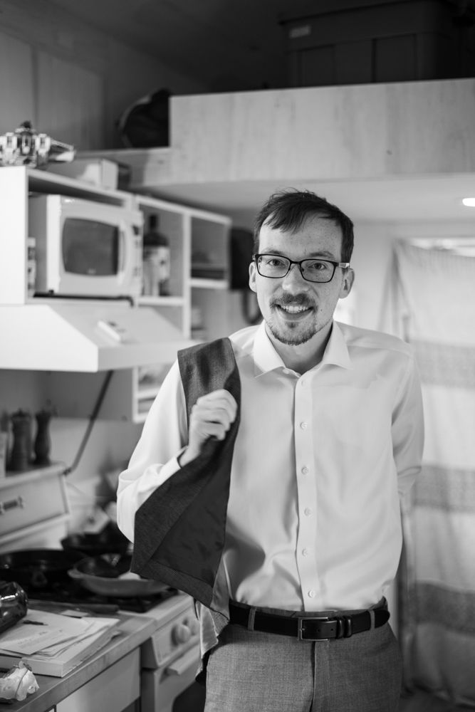 Black and white portrait of a smiling groom in glasses and button-down shirt.