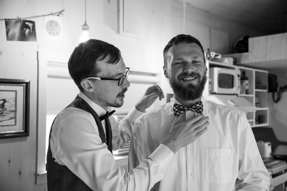 Black and white image of two people laughing while adjusting a bowtie.