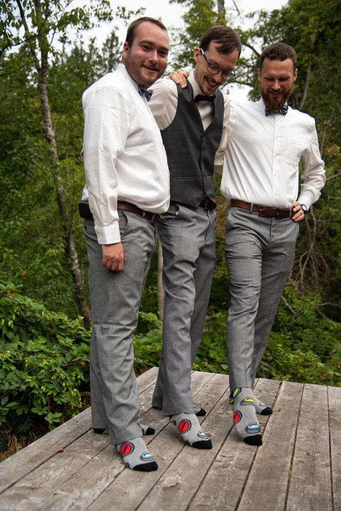 Three groomsmen in coordinated outfits showing off their matching socks on wooden deck.