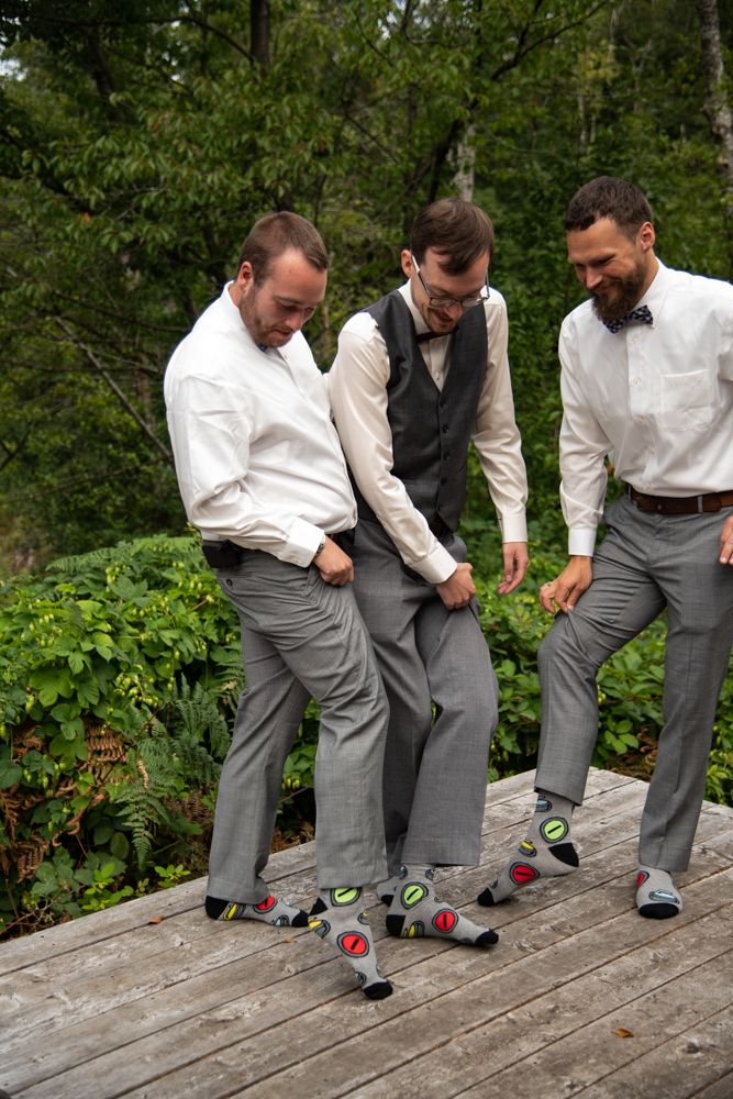 Wedding party members looking down at their matching socks on outdoor wooden deck.