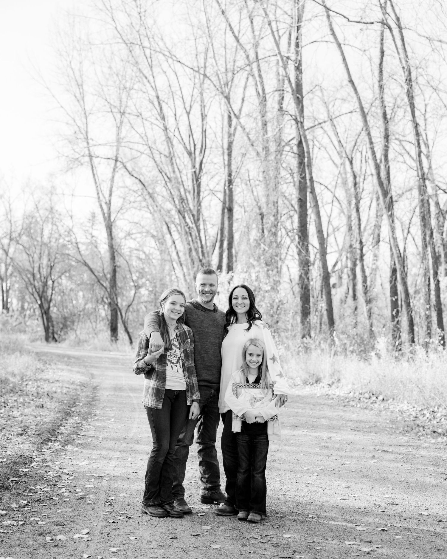A family of four poses together on a wooded path in black and white.