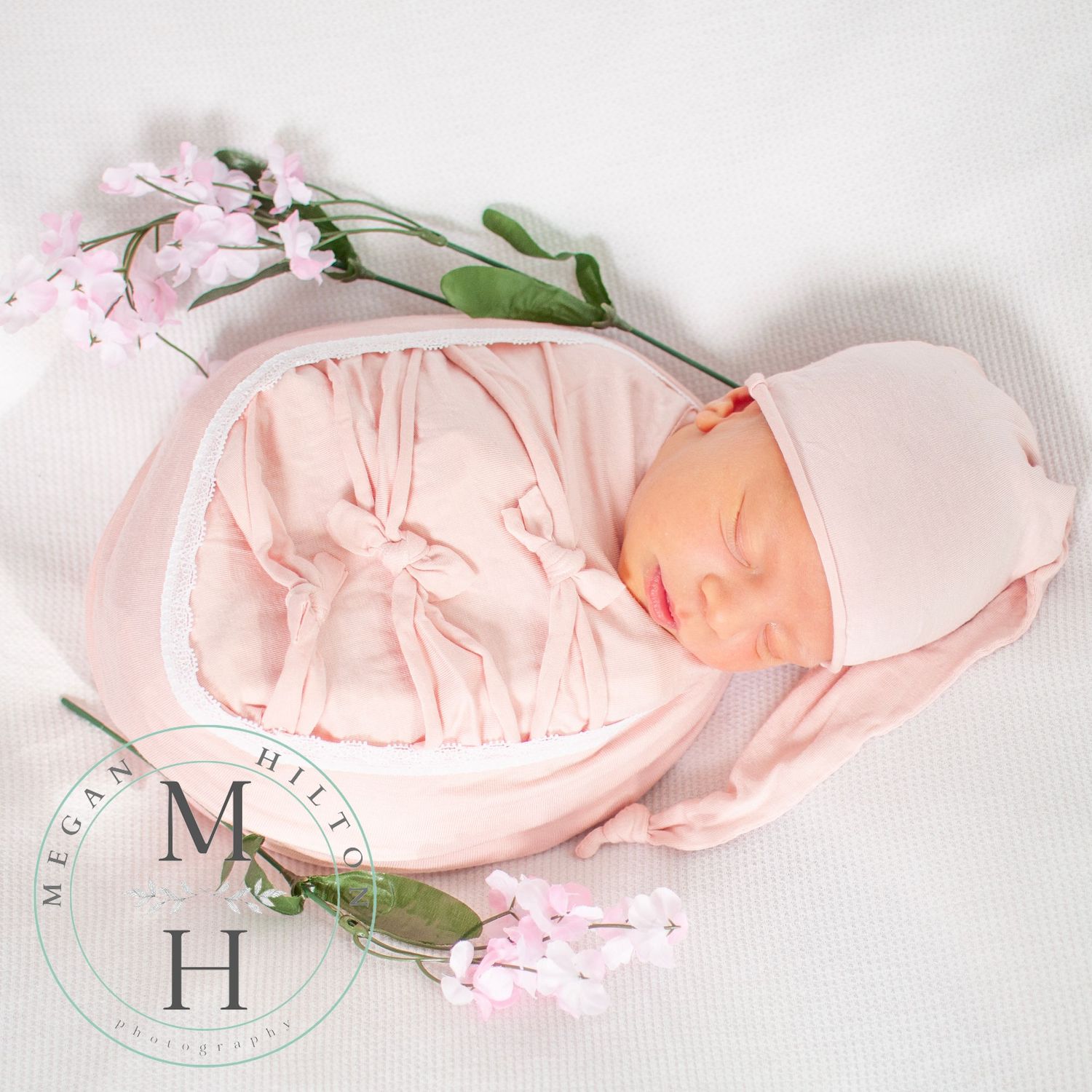 Baby newborn girl wrapped in pink surrounded by flowers on white backdrop